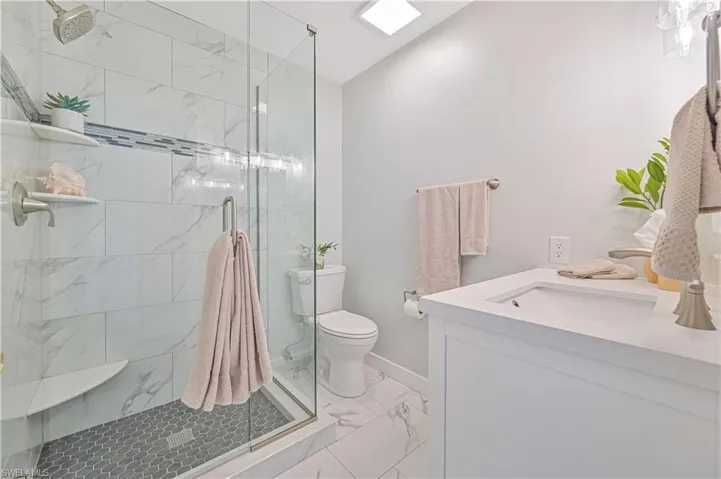 Bathroom featuring a shower with shower door, vanity, toilet, and tile floors