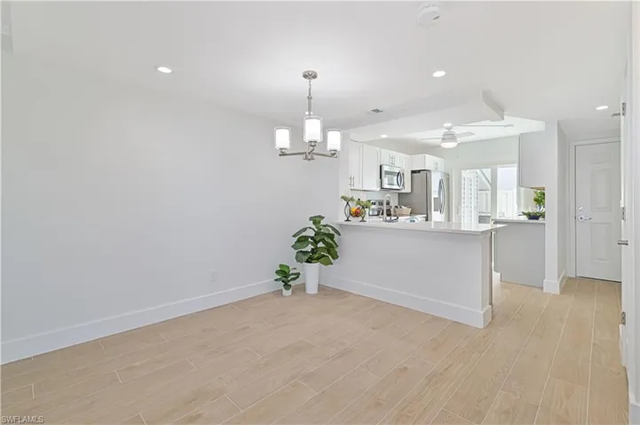 Kitchen with light hardwood / wood-style floors, ceiling fan with notable chandelier, stainless steel appliances, white cabinets, and kitchen peninsula