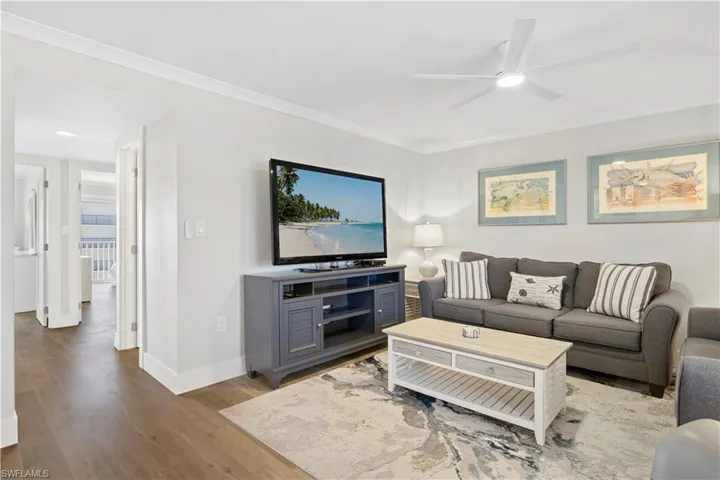 Living room with a ceiling fan, wood finished floors, and crown molding