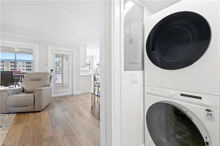 Washroom with stacked washer and clothes dryer, light wood finished floors, crown molding, and electric panel