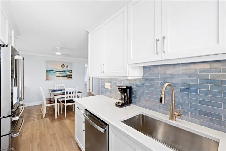 Kitchen with appliances with stainless steel finishes, tasteful backsplash, white cabinets, light wood-type flooring, and a ceiling fan