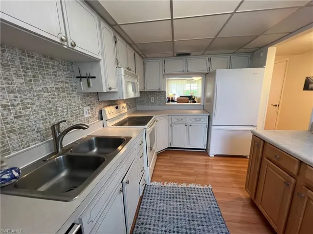 Kitchen featuring decorative backsplash, a paneled ceiling, sink, light hardwood / wood-style flooring, and white appliances