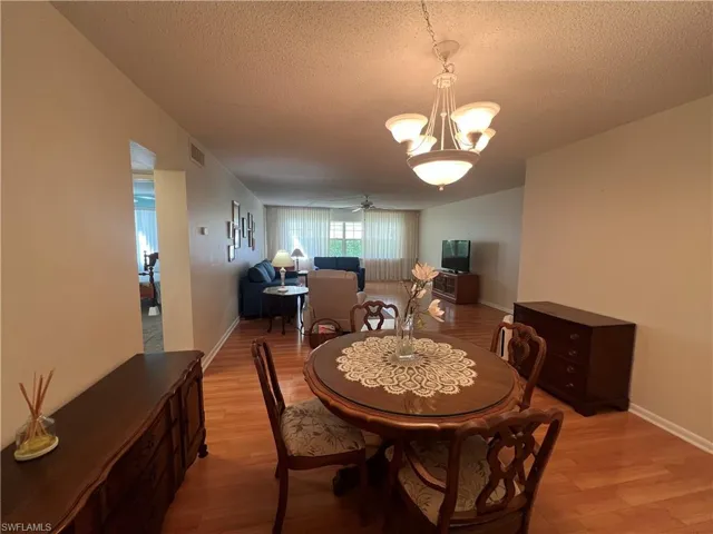 Dining room with ceiling fan with notable chandelier, a textured ceiling, and light wood-type flooring