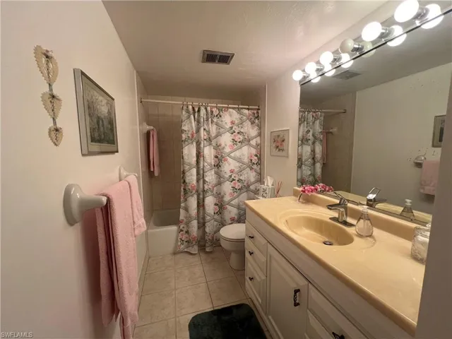 Guest bathroom featuring toilet, vanity, tile patterned floors, and shower / tub combo with curtain