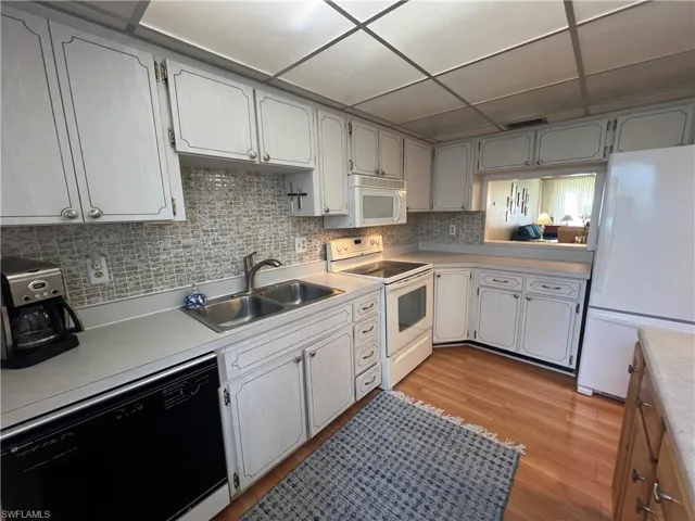 Kitchen featuring a drop ceiling, sink, backsplash, light wood-type flooring, and white appliances