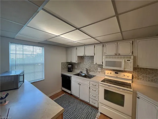 Kitchen with light hardwood / wood-style floors, a paneled ceiling, sink, backsplash, and white appliances