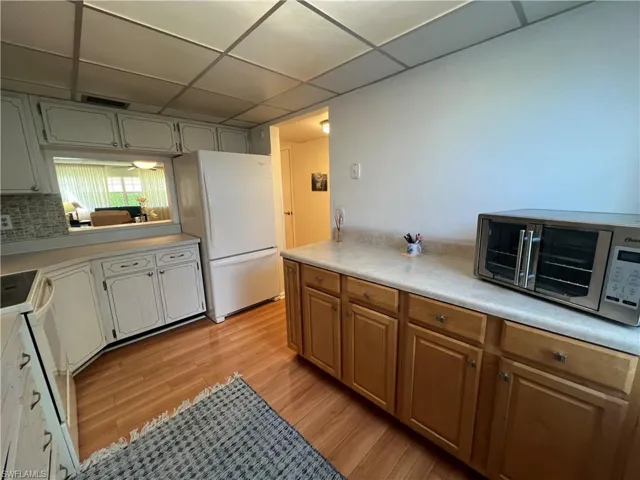 Kitchen featuring white appliances, tasteful backsplash, light wood-type flooring, and a drop ceiling