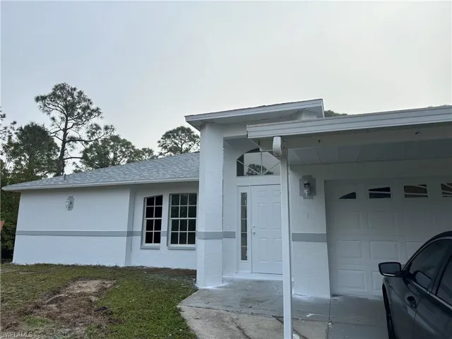Property entrance with an attached garage, stucco siding, and roof with shingles