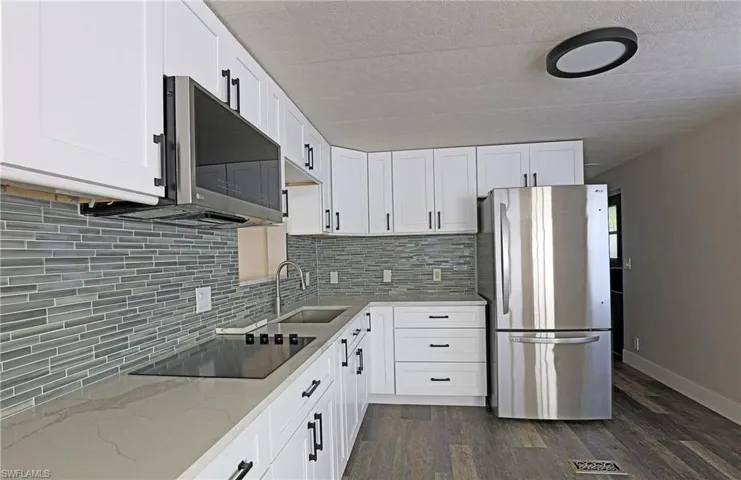 Kitchen featuring appliances with stainless steel finishes, light stone counters, white cabinetry, and dark wood finished floors