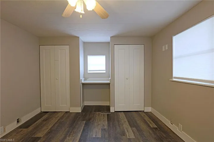 Unfurnished bedroom with multiple closets, dark wood-style floors, and a ceiling fan