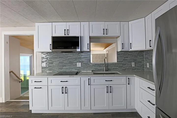 Kitchen with appliances with stainless steel finishes, white cabinetry, tasteful backsplash, wood ceiling, and vaulted ceiling