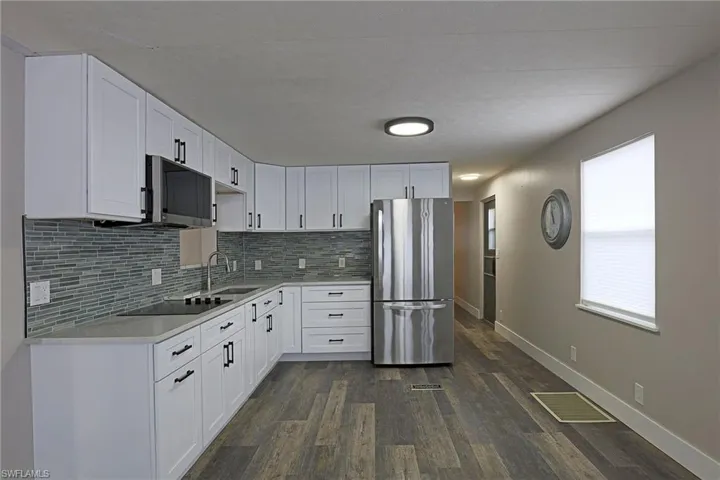 Kitchen with white cabinets, appliances with stainless steel finishes, dark wood-style flooring, light stone counters, and decorative backsplash