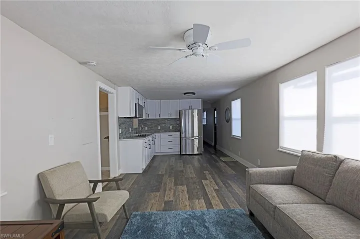 Kitchen featuring white cabinets, tasteful backsplash, freestanding refrigerator, open floor plan, and dark wood finished floors