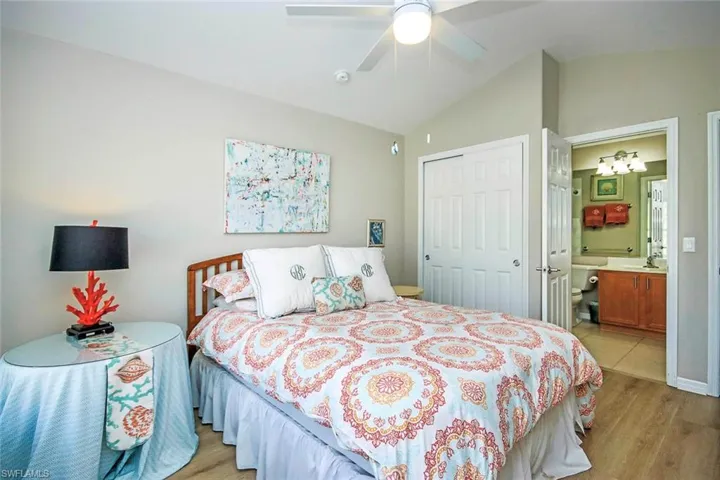 Bedroom featuring light wood-type flooring, lofted ceiling, a closet, ensuite bath, and a ceiling fan