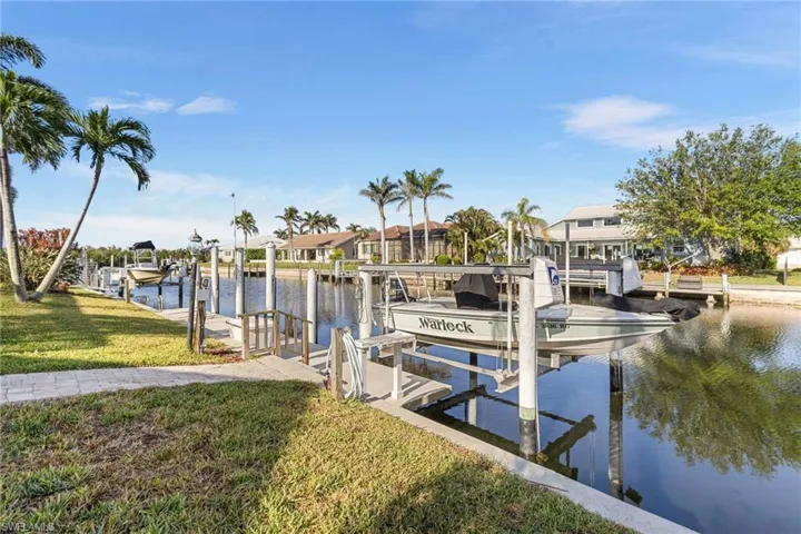 View of dock with a water view, boat lift, a yard, and a residential view