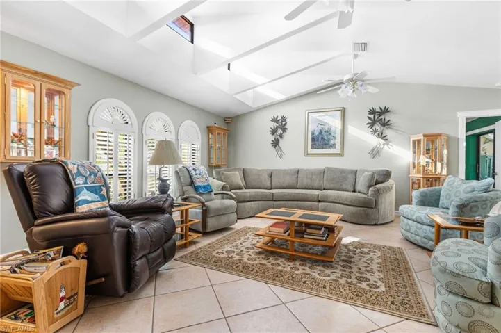 Living room featuring lofted ceiling with skylight, tile patterned flooring, visible vents, and ceiling fan