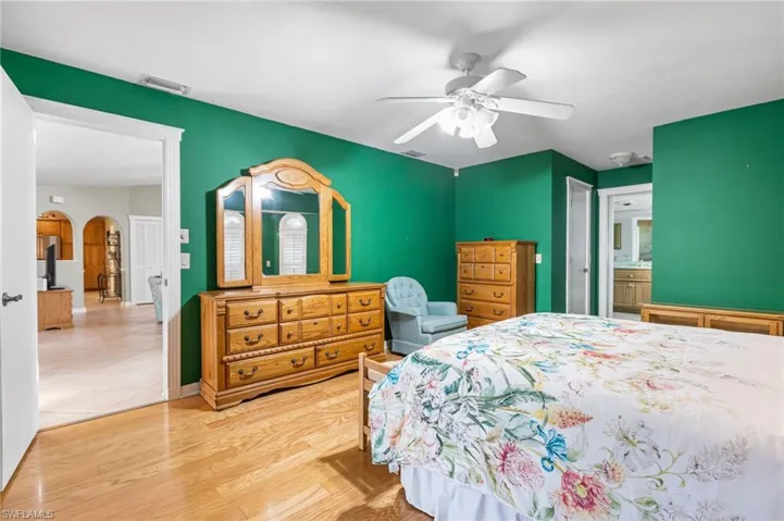 Bedroom with baseboards, arched walkways, visible vents, a ceiling fan, and wood finished floors