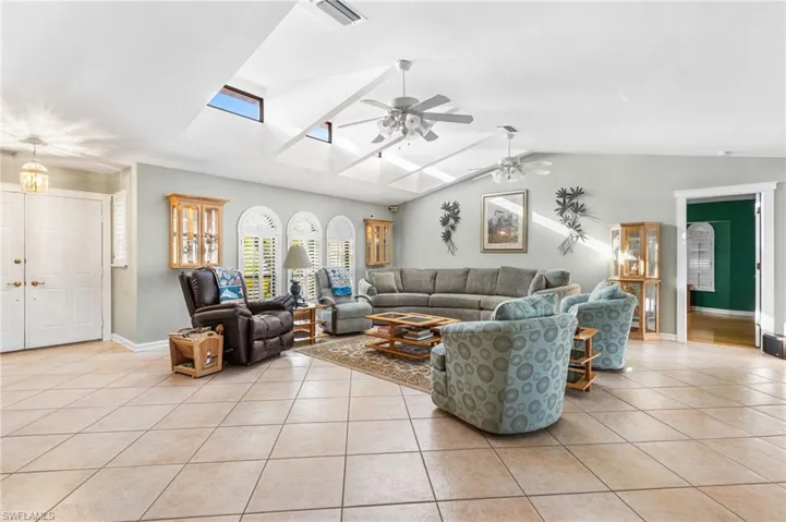 Living area with vaulted ceiling with skylight, a ceiling fan, light tile patterned floors, baseboards, and visible vents