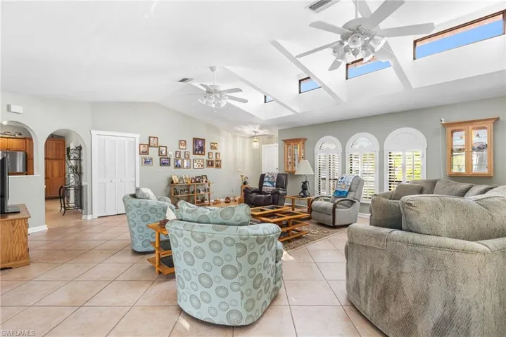 Living area featuring light tile patterned flooring, ceiling fan, visible vents, arched walkways, and lofted ceiling with skylight