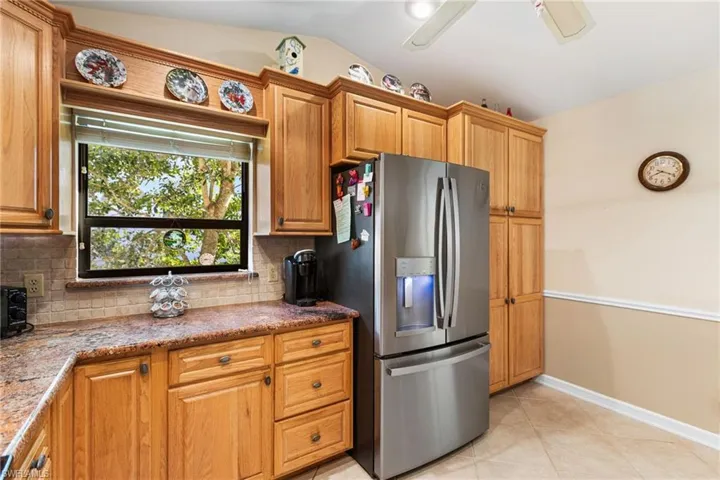 Kitchen with decorative backsplash, light tile patterned flooring, stainless steel fridge, light stone countertops, and vaulted ceiling