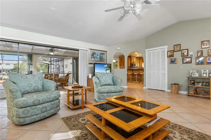 Living room with light tile patterned flooring, a ceiling fan, lofted ceiling, baseboards, and arched walkways