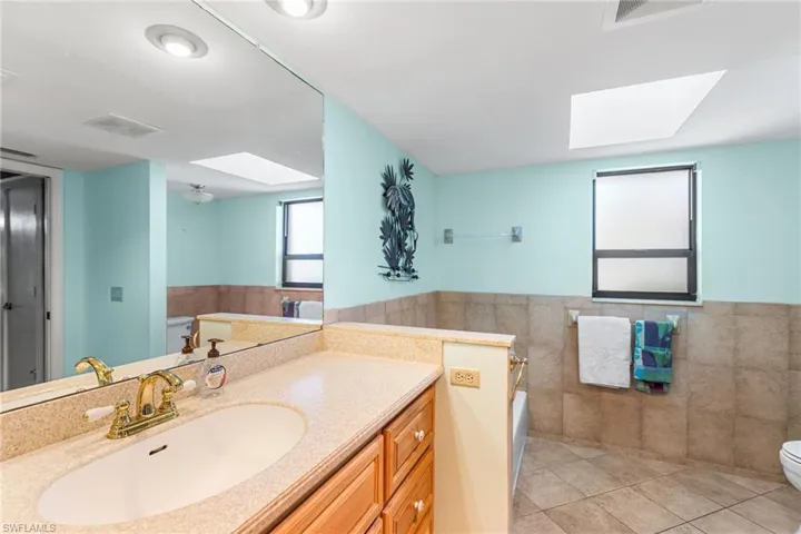 Full bath with tile walls, a skylight, toilet, tile patterned flooring, and wainscoting