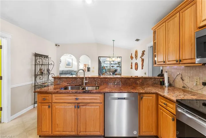 Kitchen featuring dark stone counters, appliances with stainless steel finishes, lofted ceiling, a sink, and backsplash