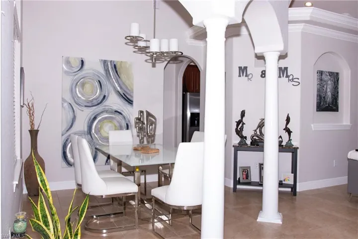 Dining room featuring tile patterned flooring, ornate columns, crown molding, and an inviting chandelier