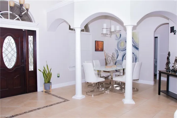 Tiled entrance foyer with ornate columns, a chandelier, and ornamental molding