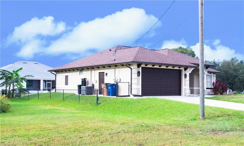 View of side of property with a yard, central AC, and a garage