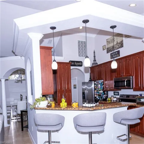 Kitchen featuring a breakfast bar, stainless steel appliances, hanging light fixtures, and dark stone counters