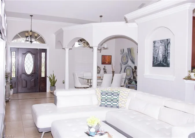 Foyer entrance featuring decorative columns, light tile patterned floors, crown molding, and an inviting chandelier