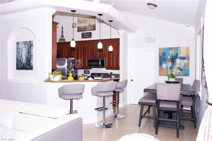 Kitchen featuring high vaulted ceiling, crown molding, light tile patterned floors, decorative light fixtures, and stainless steel appliances