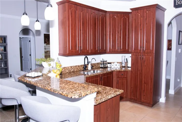 Kitchen featuring ornamental molding, sink, light tile patterned floors, decorative light fixtures, and stone counters