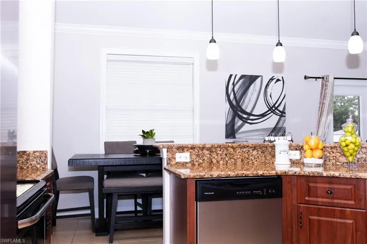 Kitchen with light stone countertops, ornamental molding, pendant lighting, and appliances with stainless steel finishes
