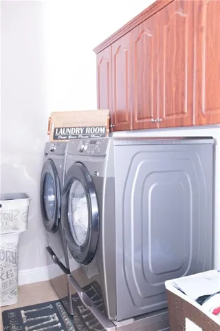 Laundry area with washer and dryer, tile patterned flooring, and cabinets