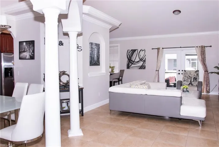 Tiled living room featuring ornate columns, crown molding, and french doors