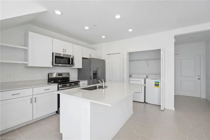 Kitchen featuring white cabinetry, stainless steel appliances, a center island with sink, open shelves, and light tile patterned floors