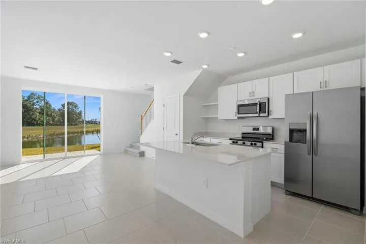 Kitchen featuring stainless steel appliances, a water view, white cabinetry, light stone countertops, and an island with sink
