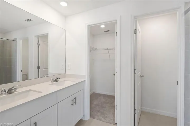 Full bath featuring double vanity, a spacious closet, light tile patterned floors, a shower stall, and light colored carpet