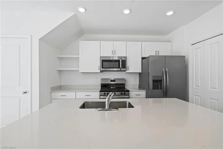 Kitchen featuring appliances with stainless steel finishes, open shelves, white cabinets, light stone counters, and recessed lighting