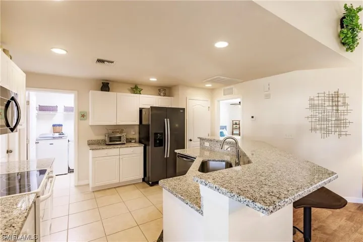 Kitchen with an island with sink, appliances with stainless steel finishes, recessed lighting, white cabinets, and light stone counters