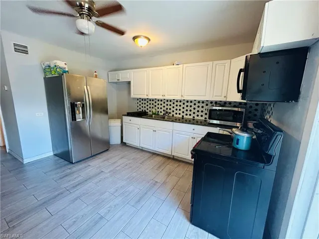 Kitchen Unit featuring tasteful backsplash, visible vents, light wood-style floors, white cabinets, and black stove and a stainless steel 2 door refrigerator.