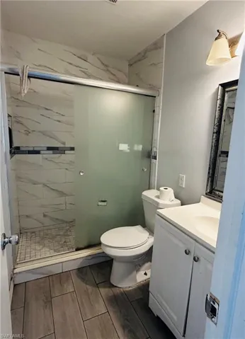 Full bath with toilet, a stall shower, wood finish floors, and vanity