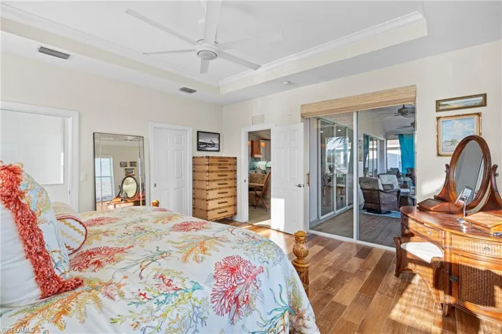 Bedroom with a raised ceiling, hardwood / wood-style floors, access to exterior, and ceiling fan