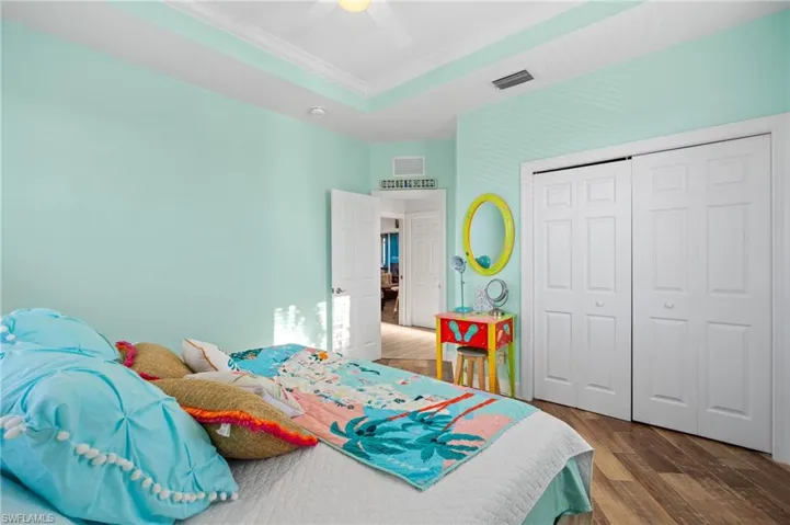 Bedroom with hardwood / wood-style floors, ceiling fan, a raised ceiling, crown molding, and a closet