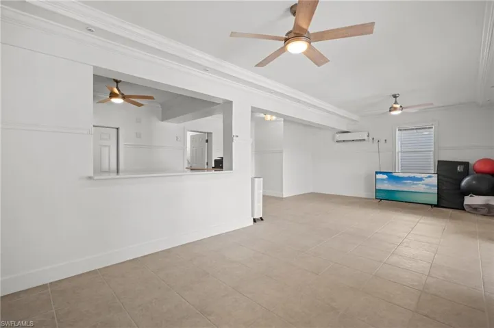 Unfurnished living room featuring ornamental molding, a wall unit AC, and light tile patterned floors