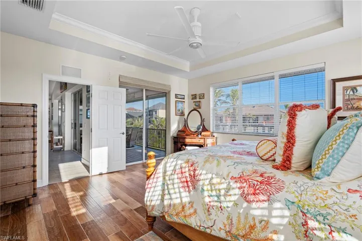 Bedroom featuring wood-type flooring, ornamental molding, a tray ceiling, ceiling fan, and access to exterior