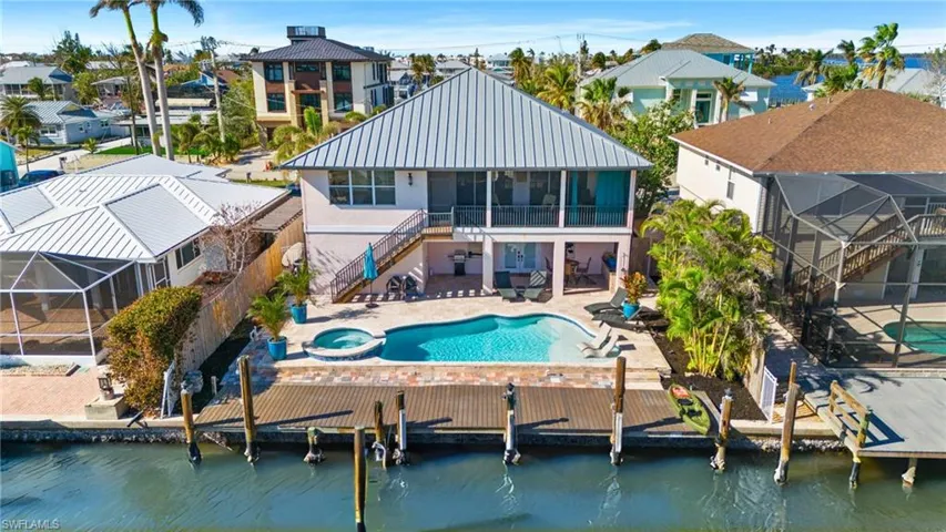 Rear view of property with a swimming pool with hot tub, a water view, a sunroom, and a patio area