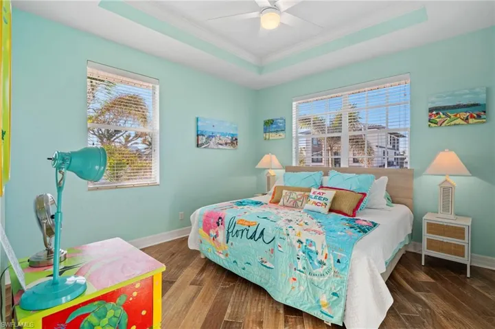 Bedroom featuring dark wood-type flooring, ceiling fan, a tray ceiling, and multiple windows